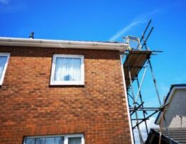 Vue de profil d'une maison résidentielle construite en briques avec un échafaudage sur le côté, près du toit, impliquant le besoin d'un maçon ou d'un couvreur.