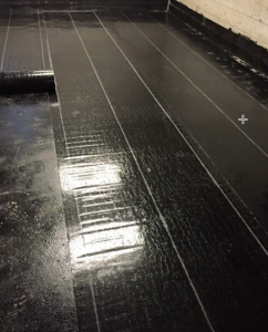 Plusieurs rouleaux de membrane élastomère noire déroulés sur un toit plat